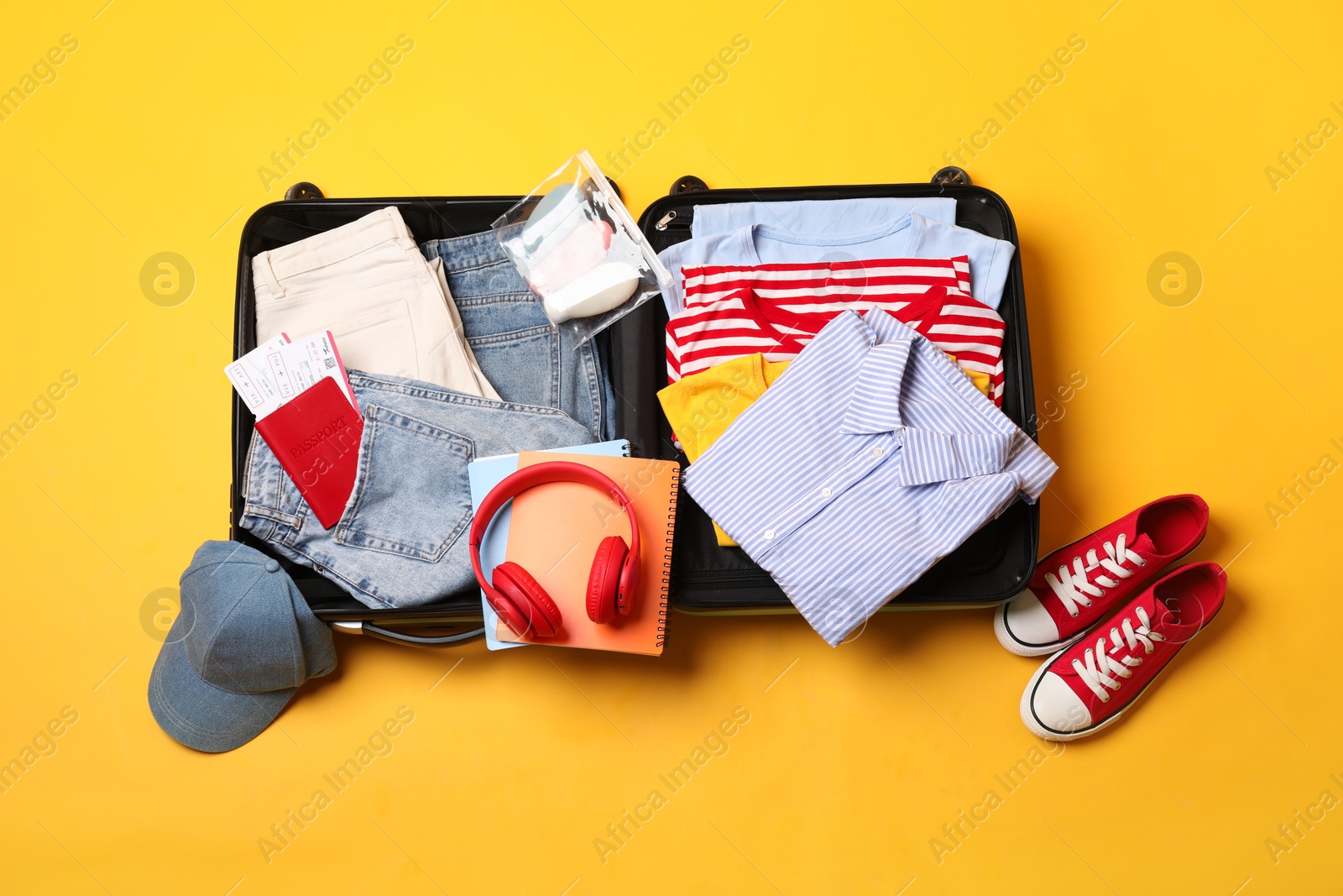 Photo of Open suitcase with traveler's belongings on yellow background, flat lay