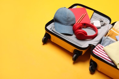 Photo of Open suitcase with traveler's belongings on yellow background, space for text