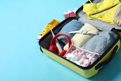 Photo of Open suitcase with traveler's belongings on light blue background, space for text