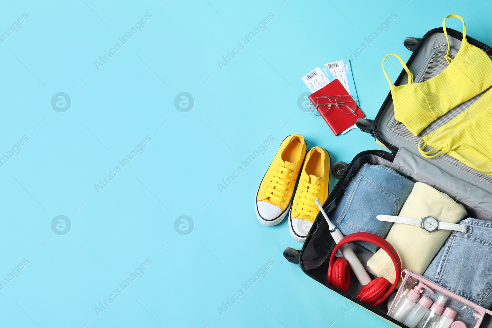 Photo of Open suitcase with traveler's belongings on light blue background, flat lay. Space for text