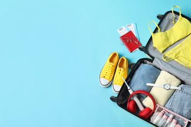 Photo of Open suitcase with traveler's belongings on light blue background, flat lay. Space for text