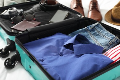 Open suitcase with traveler's belongings on bed, closeup