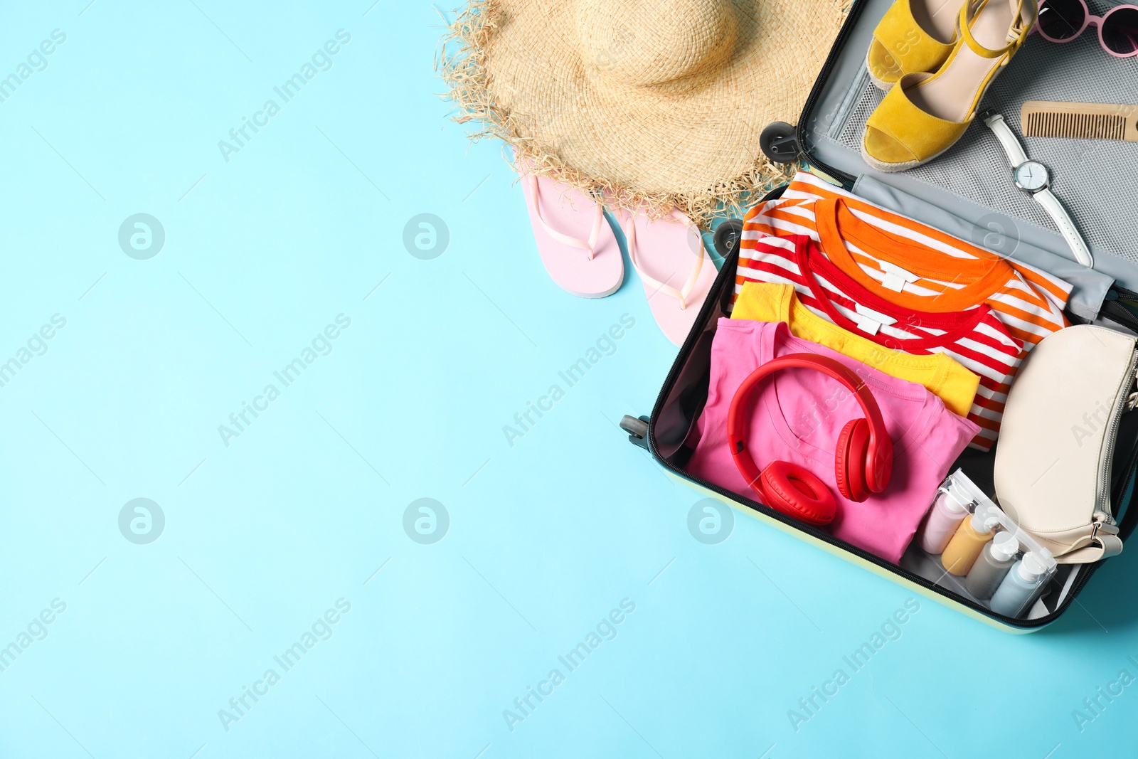 Photo of Open suitcase with traveler's belongings on light blue background, flat lay. Space for text