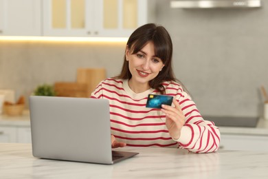 Online banking. Smiling woman with credit card and laptop paying purchase at table indoors