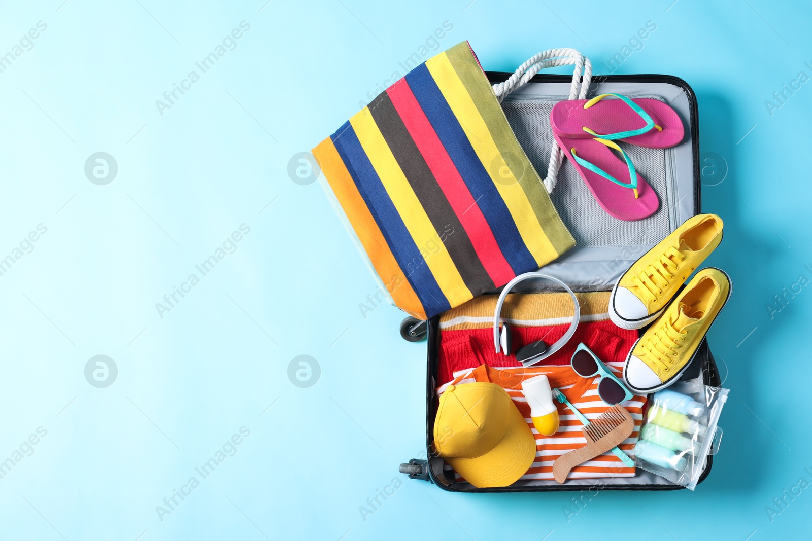 Photo of Open suitcase with traveler's belongings on light blue background, top view. Space for text