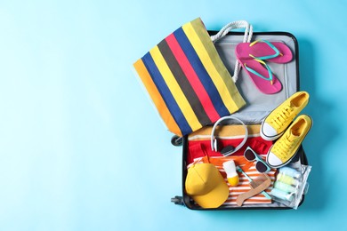 Photo of Open suitcase with traveler's belongings on light blue background, top view. Space for text