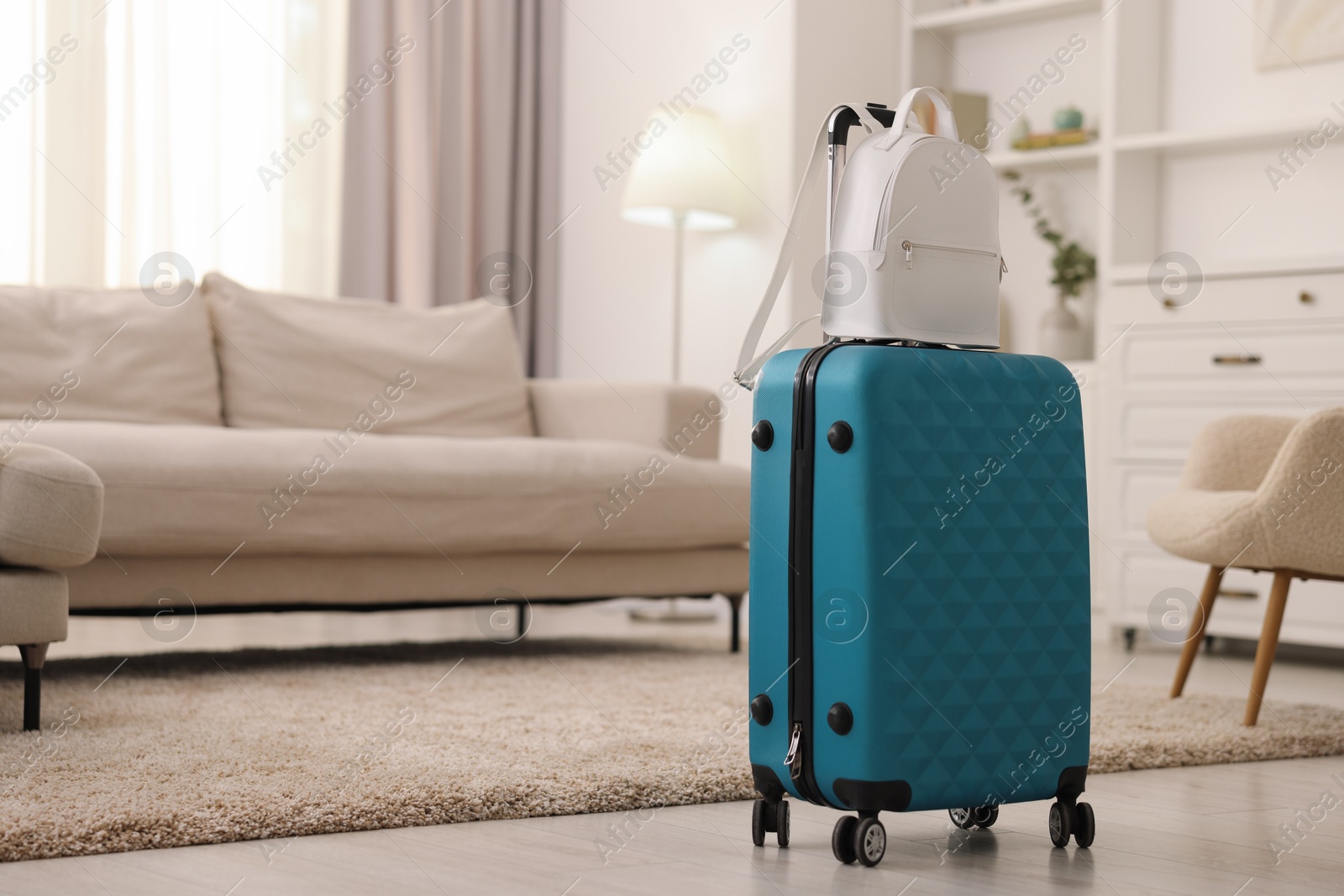 Photo of Light blue suitcase and backpack at home. Space for text