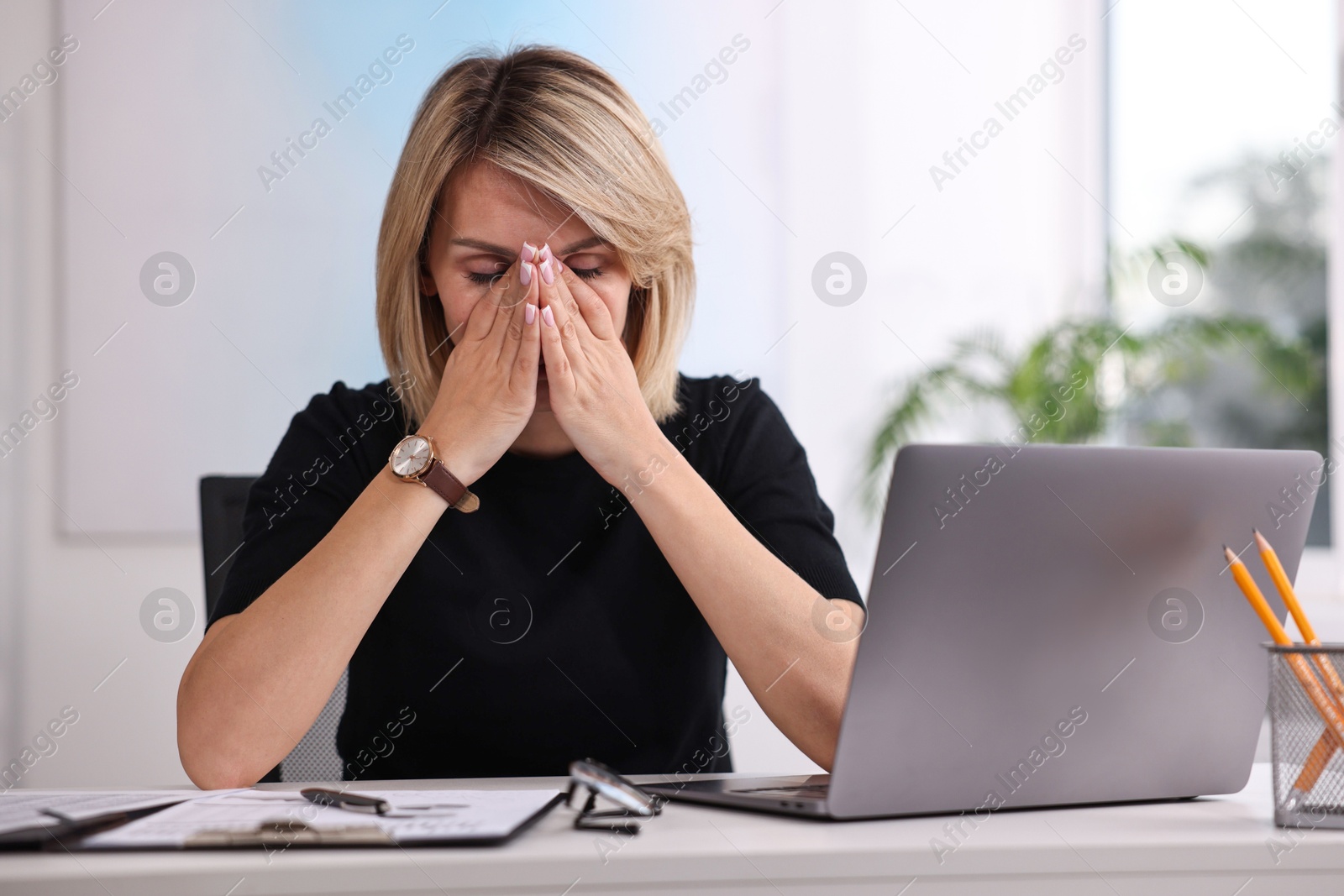 Photo of Overwhelmed woman sitting at table with laptop and documents in office