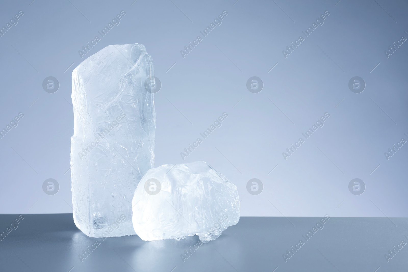 Photo of Pieces of clear ice on light grey table. Space for text