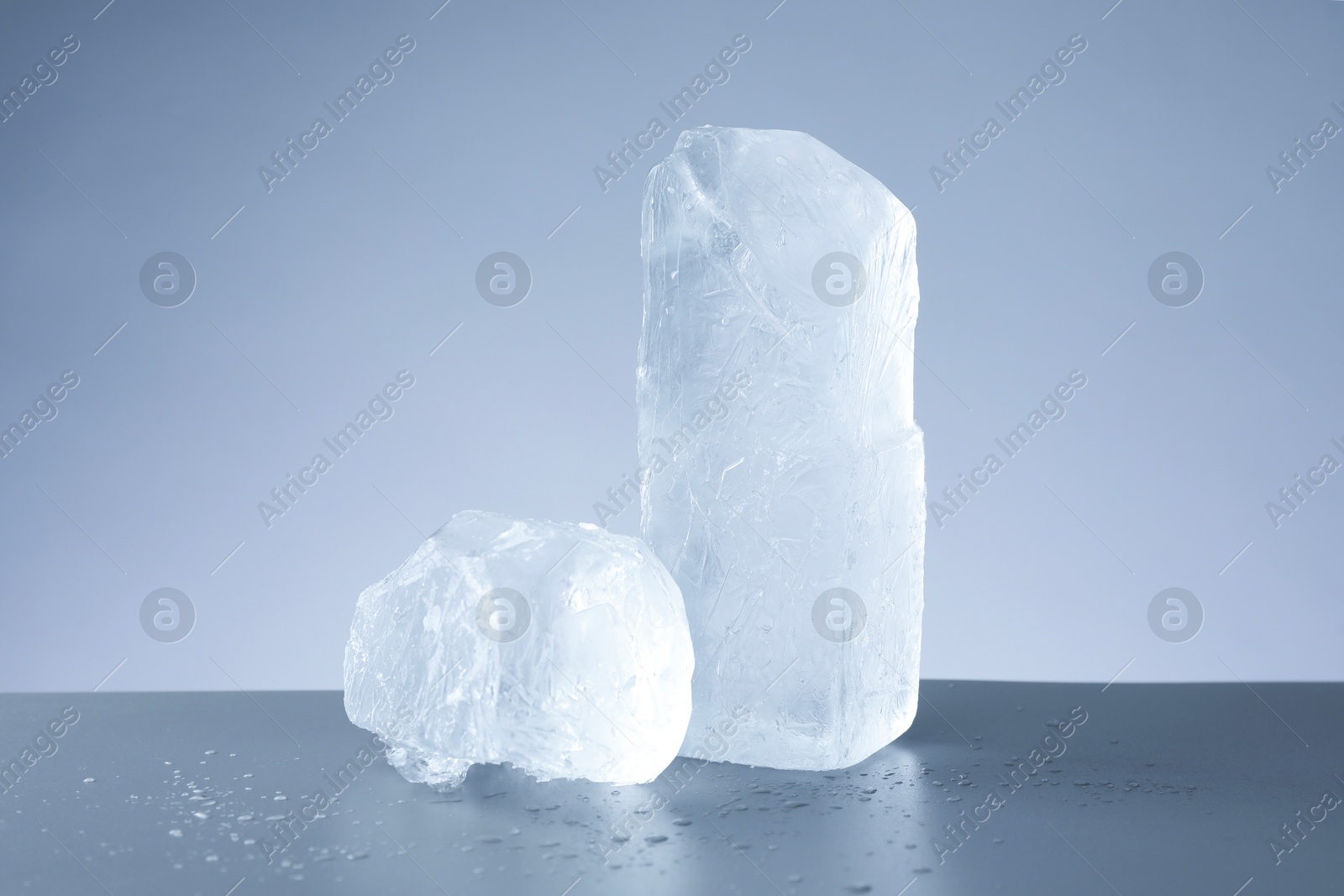 Photo of Pieces of clear ice and water drops on light grey table