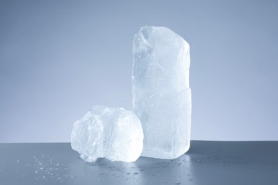 Pieces of clear ice and water drops on light grey table