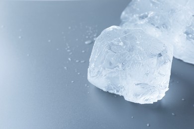 Photo of Pieces of clear ice and water drops on light grey table, closeup. Space for text