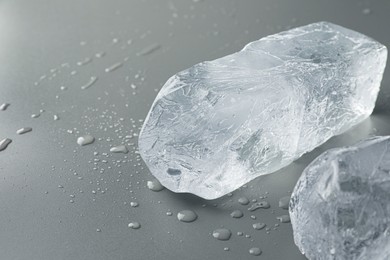 Photo of Pieces of clear ice and water drops on light grey table, closeup