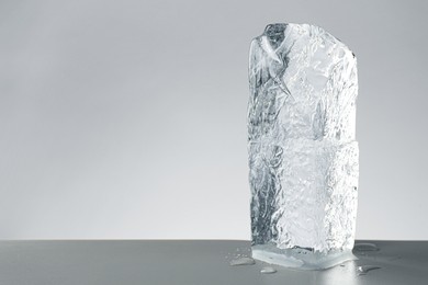 Photo of Piece of clear ice and water drops on light grey table. Space for text