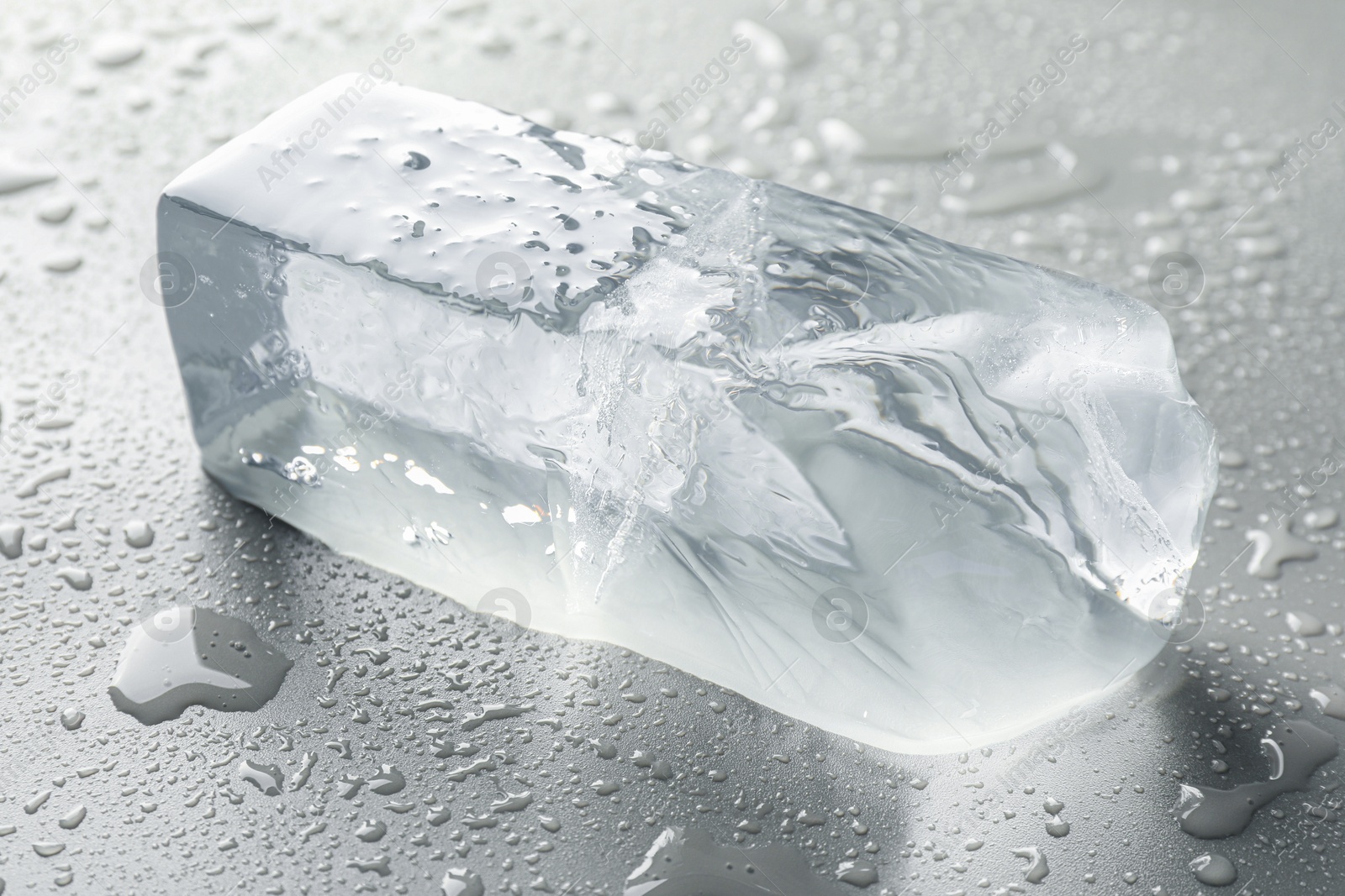 Photo of Piece of clear ice and water drops on light grey table