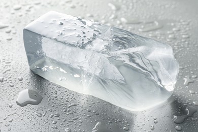 Piece of clear ice and water drops on light grey table