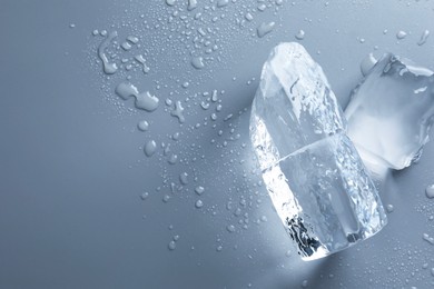 Pieces of clear ice and water drops on light grey table, top view. Space for text