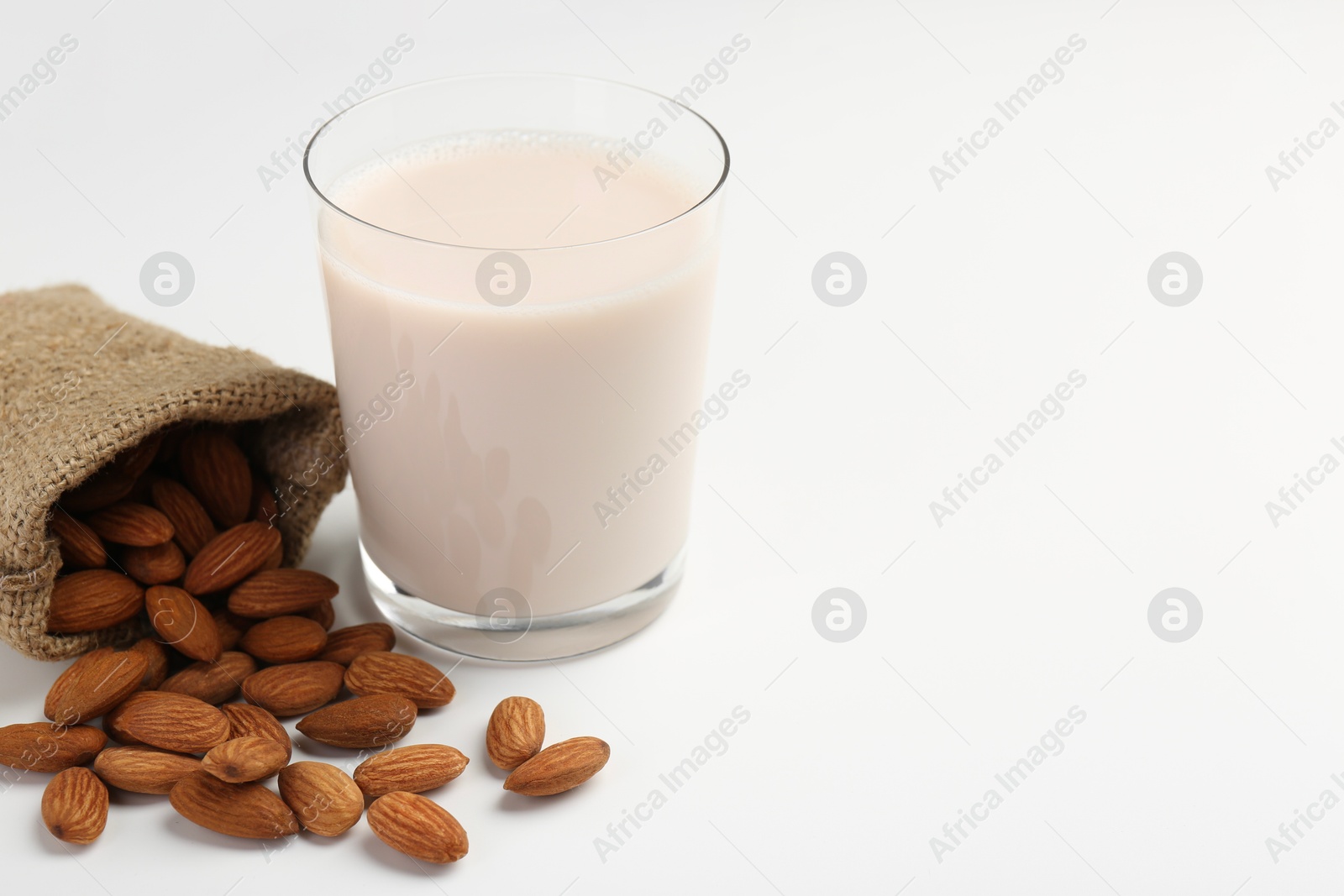 Photo of Fresh almond milk in glass, nuts and burlap sack on white background, space for text