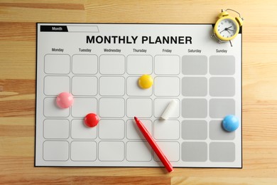 Timetable. Monthly planner, felt pen, drawing pins and alarm clock on wooden table, top view