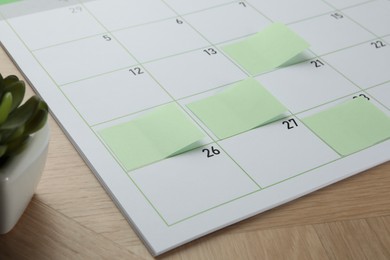 Photo of Timetable. Calendar page with green sticky notes on wooden table, closeup