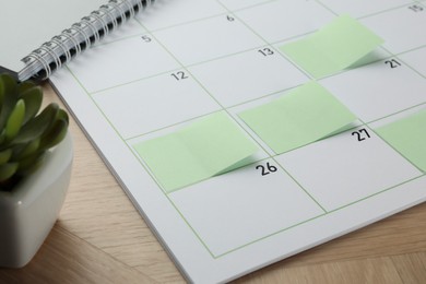 Photo of Timetable. Calendar page with green sticky notes on wooden table, closeup