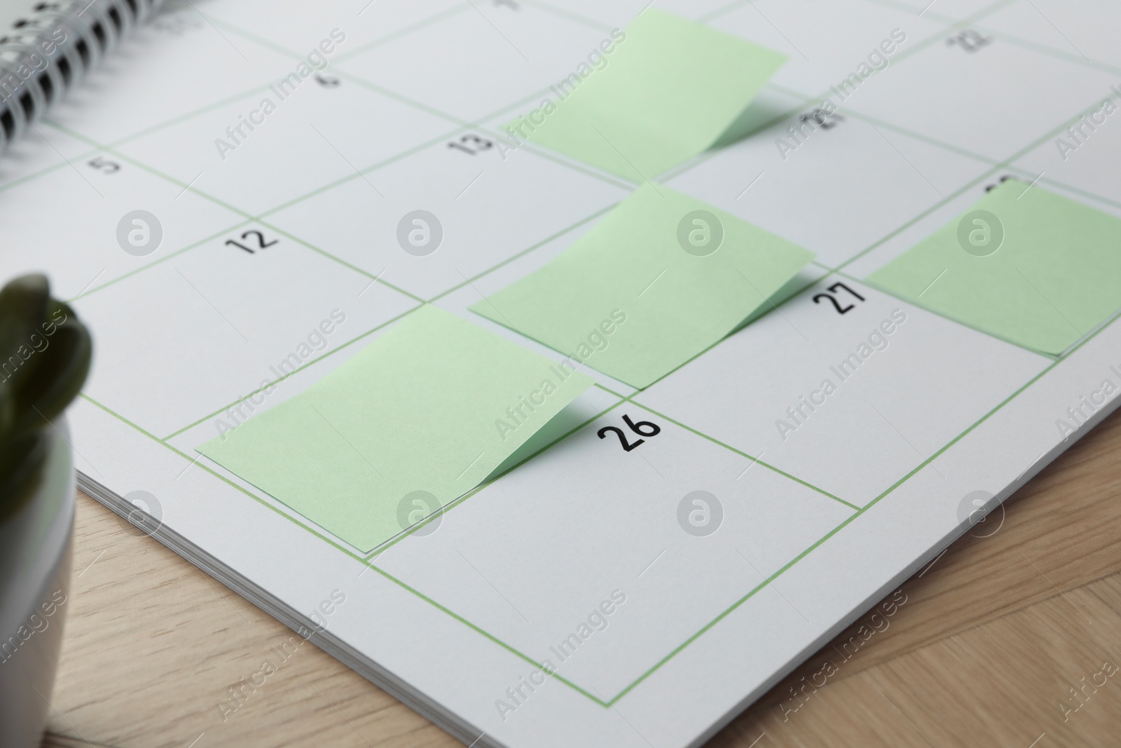 Photo of Timetable. Calendar page with green sticky notes on wooden table, closeup