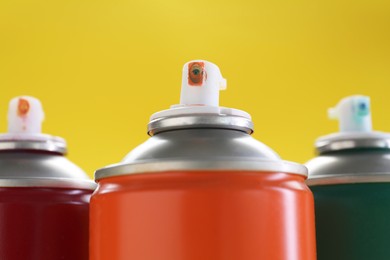 Many spray paint cans on yellow background, closeup