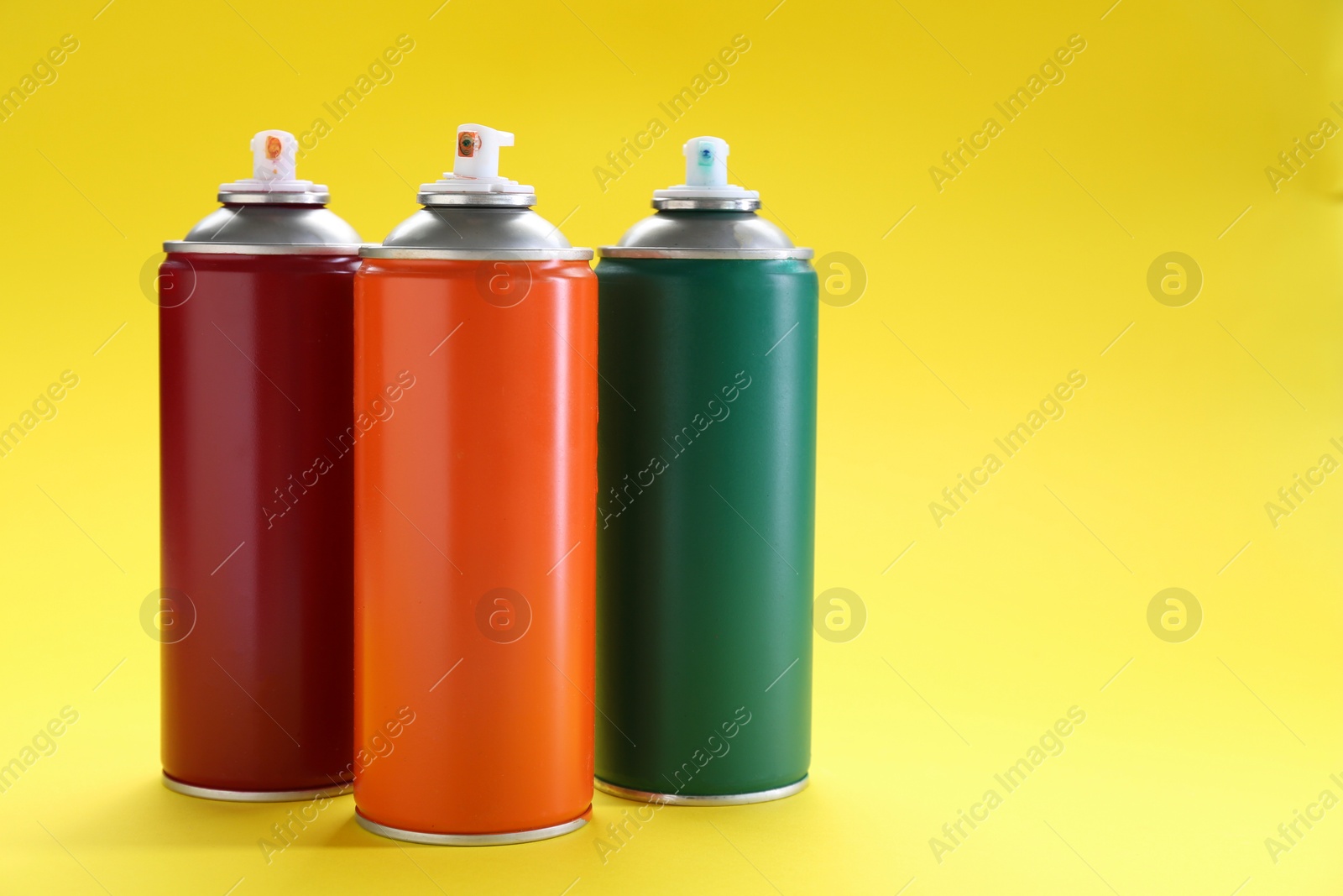 Photo of Three spray paint cans on yellow background, space for text