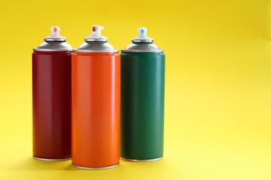 Photo of Three spray paint cans on yellow background, space for text