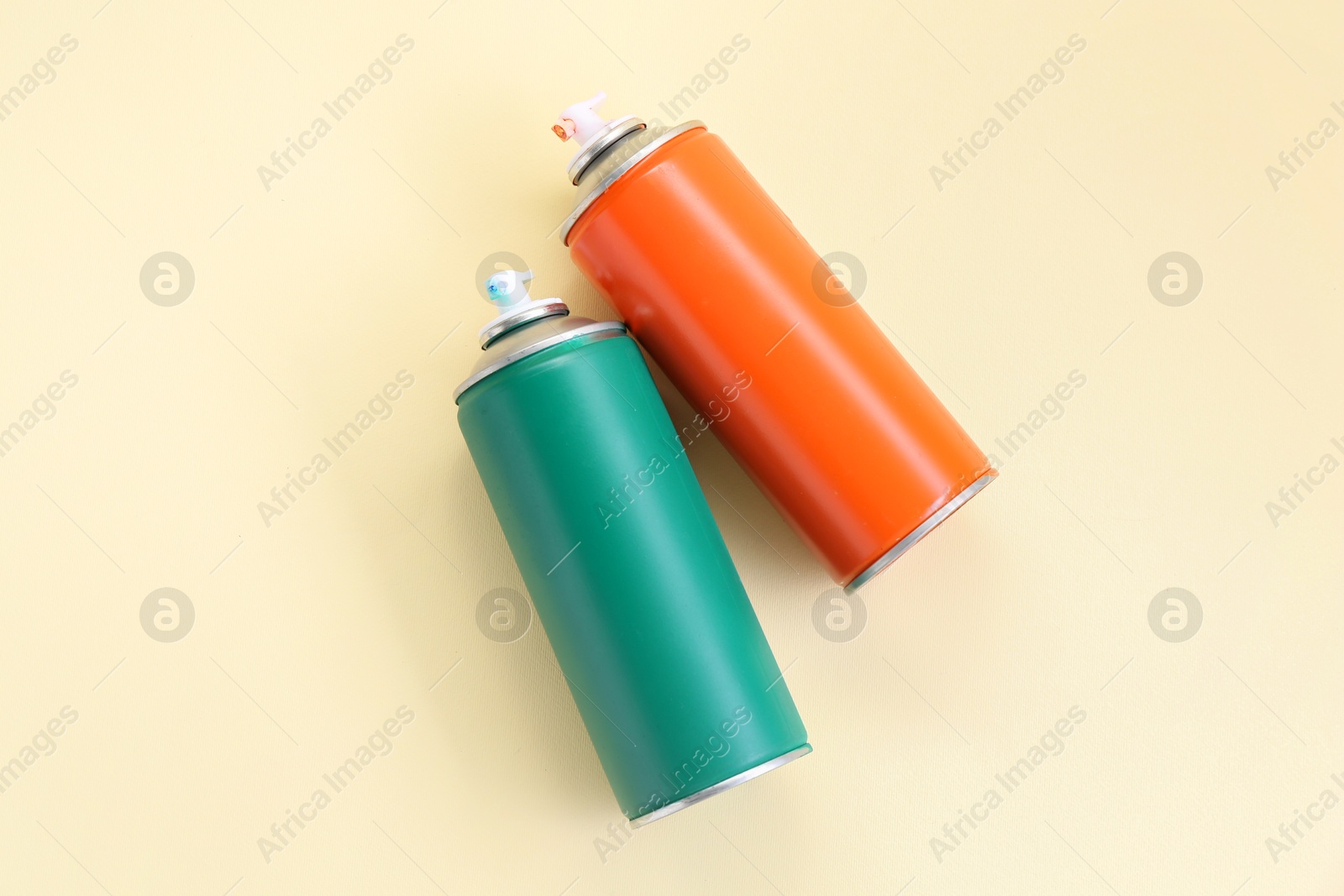 Photo of Spray paint cans on beige background, top view