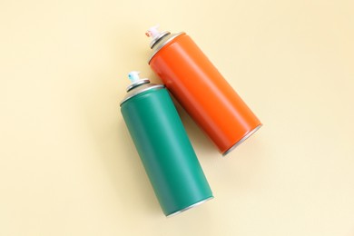 Spray paint cans on beige background, top view