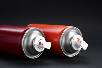 Two spray paint cans on dark gray background, closeup