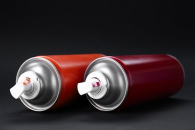 Two spray paint cans on dark gray background, closeup