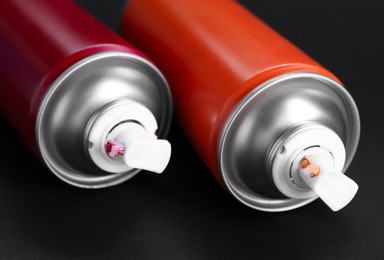 Two spray paint cans on dark gray background, closeup