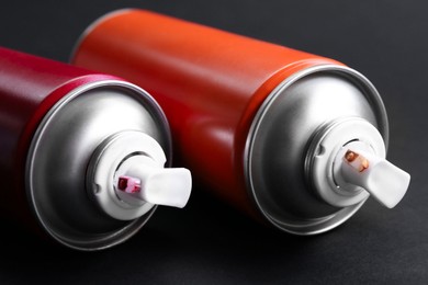 Two spray paint cans on dark gray background, closeup