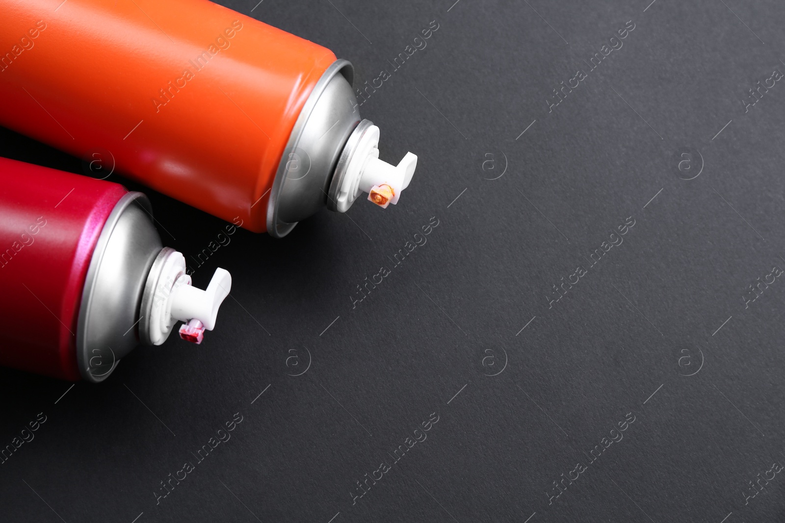 Photo of Two spray paint cans on dark gray background, top view. Space for text