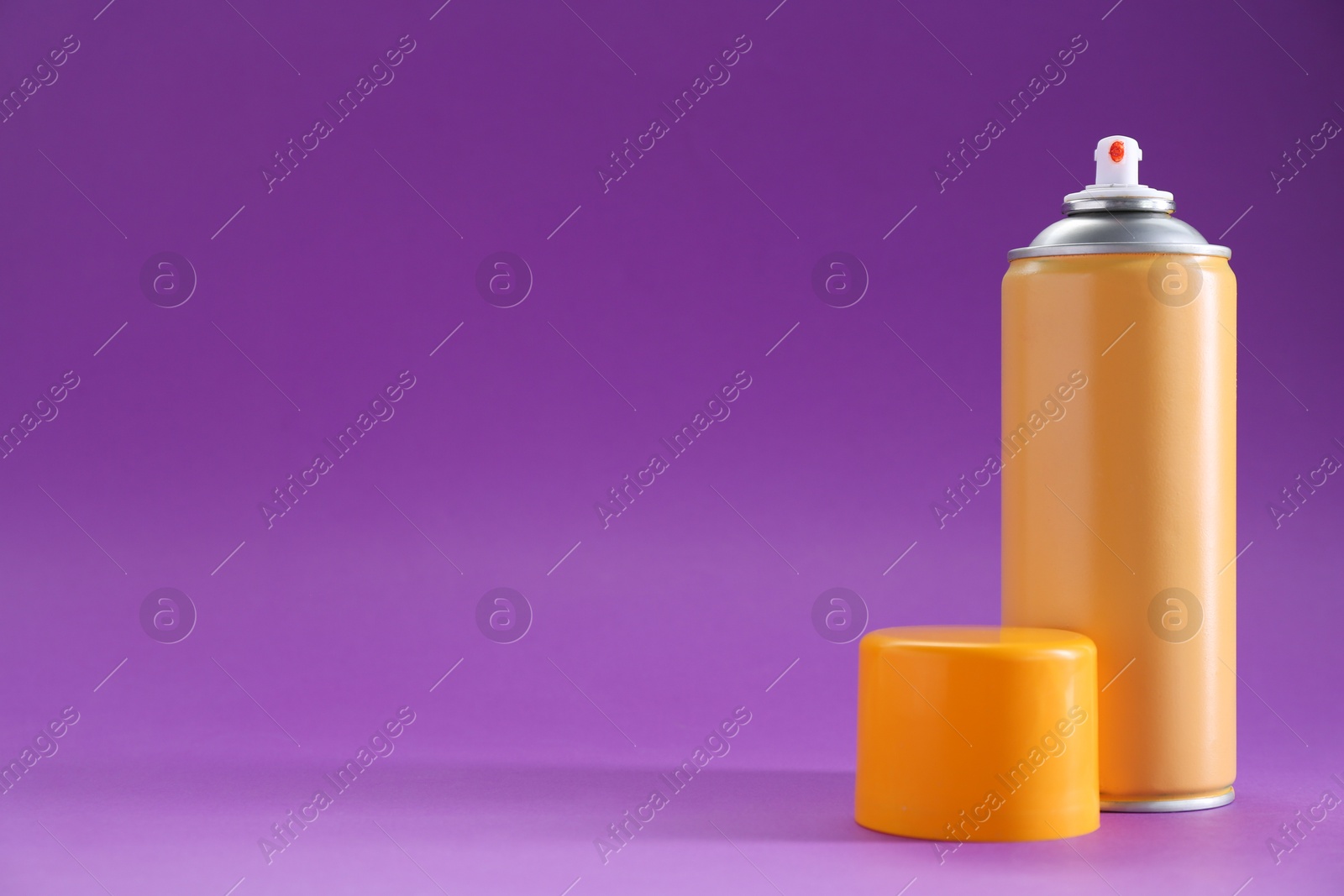 Photo of Orange spray paint can on violet background, space for text