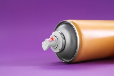 Orange spray paint can on violet background, closeup. Space for text