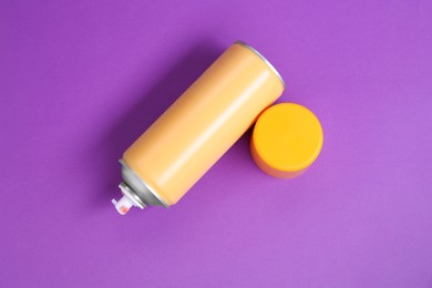 Orange spray paint can on violet background, top view