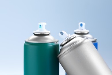 Many spray paint cans on light gray background, closeup