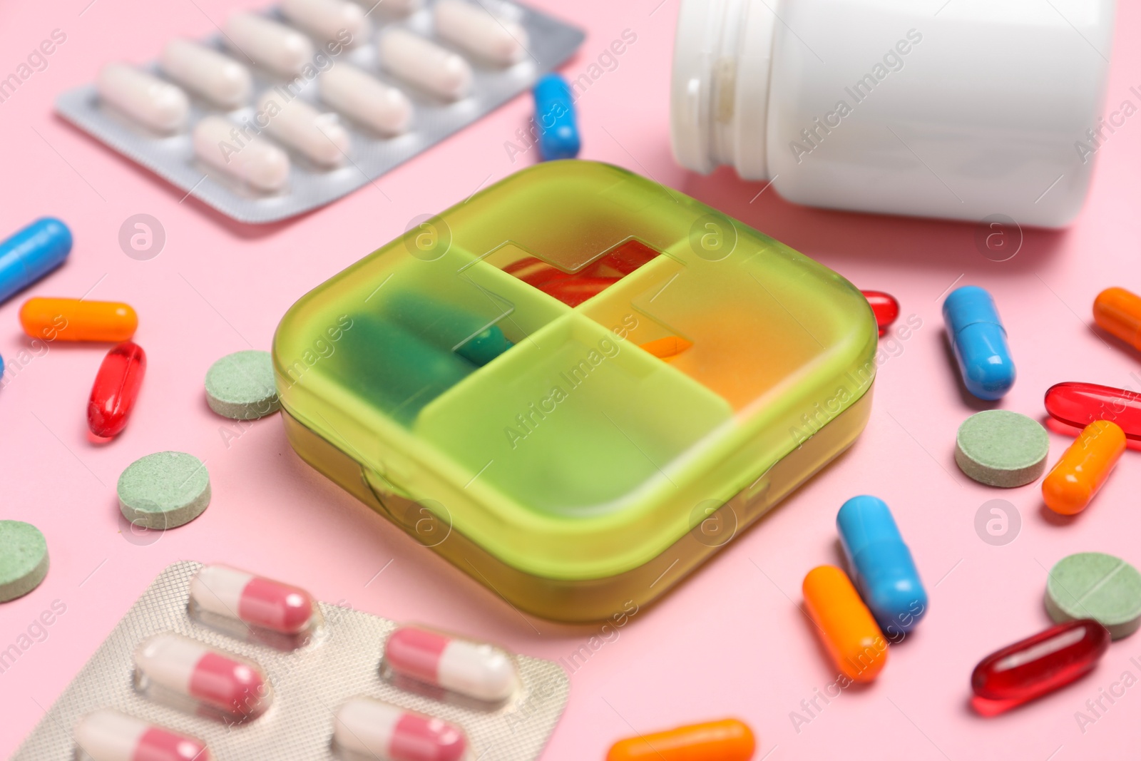 Photo of Different pills, organizer and medical jar on pink background, closeup