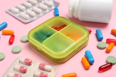 Photo of Different pills, organizer and medical jar on pink background, closeup