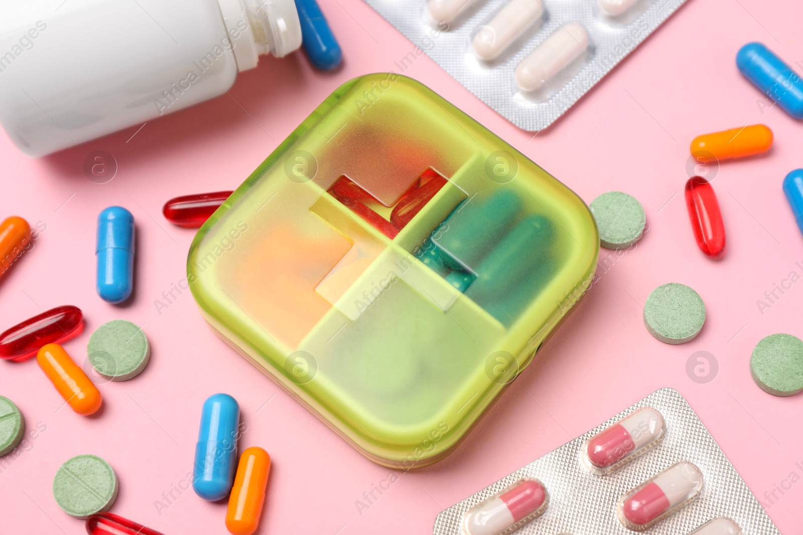 Photo of Different pills, organizer and medical jar on pink background, closeup