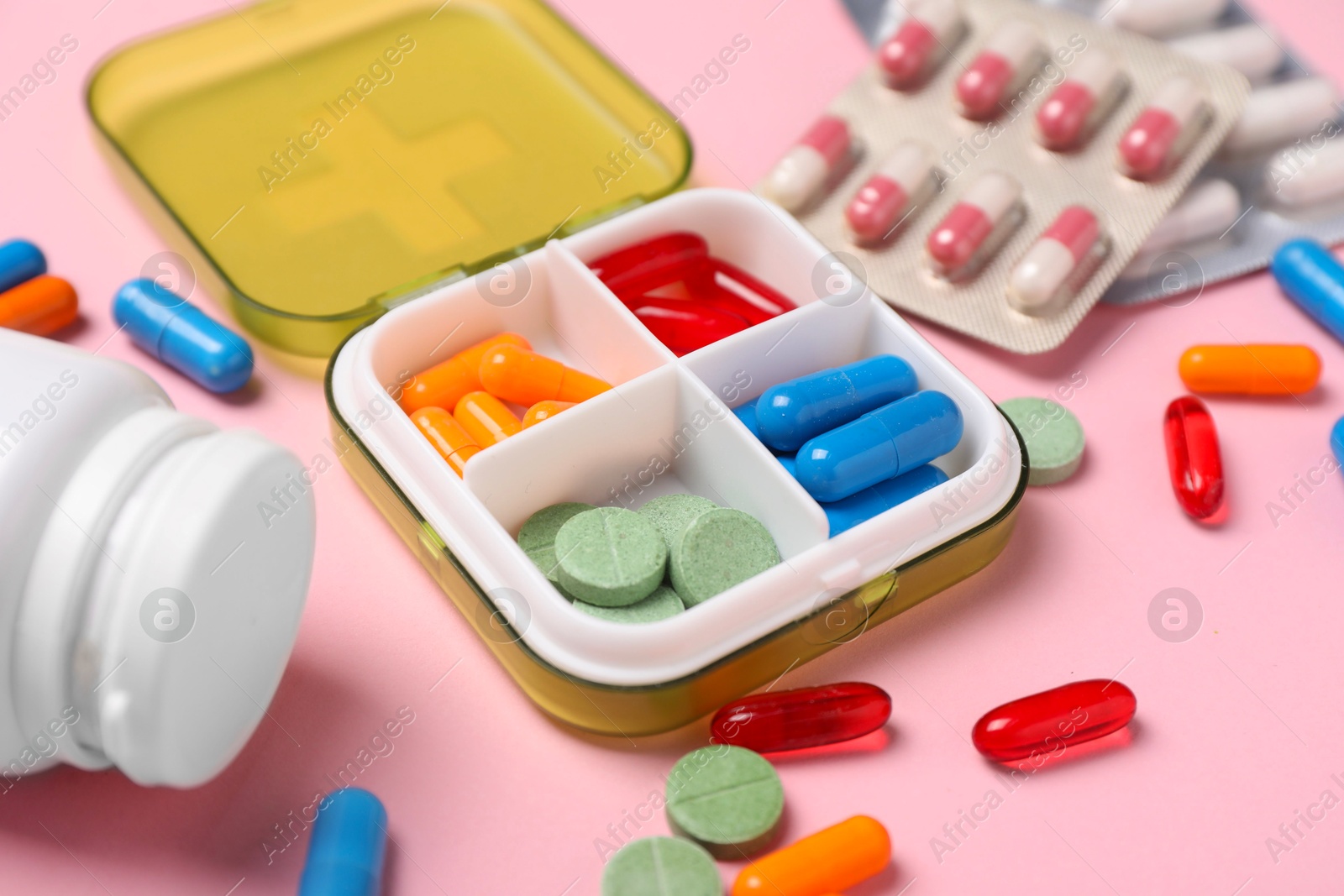 Photo of Different pills, organizer and medical jar on pink background, closeup