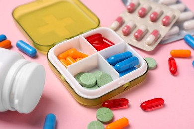 Photo of Different pills, organizer and medical jar on pink background, closeup