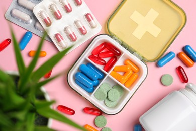 Photo of Different pills, organizer, medical jar and houseplant on pink background, flat lay