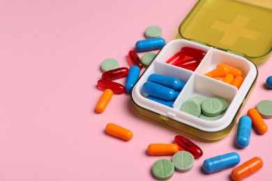 Photo of Different pills and organizer on pink background, closeup. Space for text