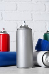 Photo of Cans of spray paint on wooden table near white brick wall