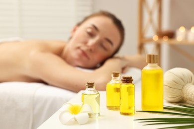 Aromatherapy. Woman relaxing on massage couch in spa salon, focus on bottles of essential oils, herbal bag and plumeria flower