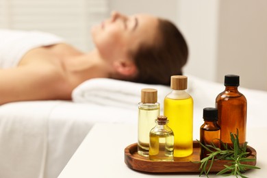 Aromatherapy. Woman relaxing on massage couch in spa salon, focus on bottles of essential oils and rosemary